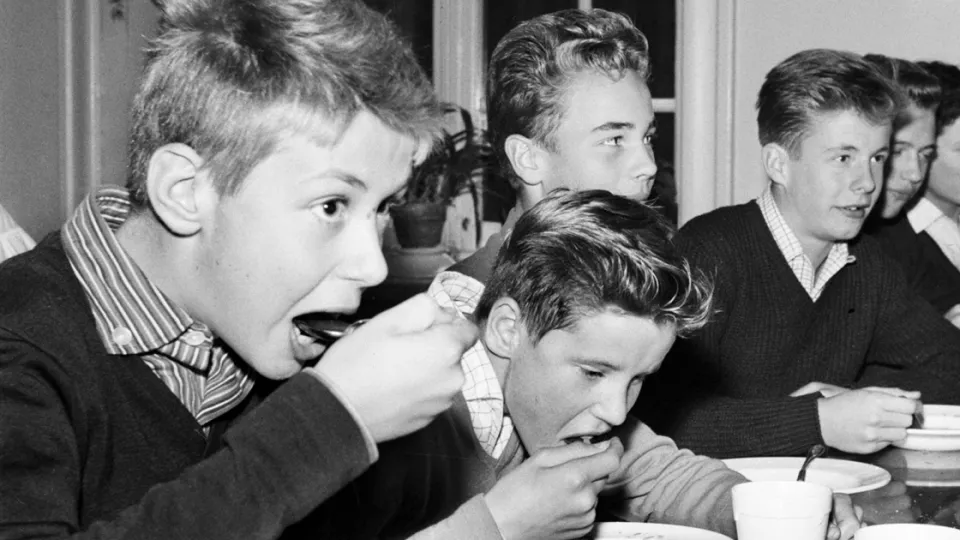 Kids eating school lunch at table, black and white image from 1950s