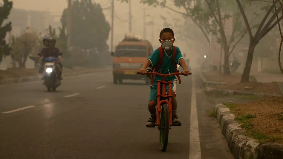 Boy cycling to school in smog in Indonesia