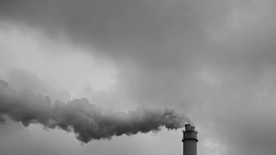 A black-and-white photo of smoke coming out an industrial chimney. Photo: Unsplash.