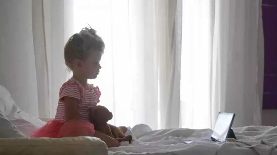 Child on bed with screen. Photo.