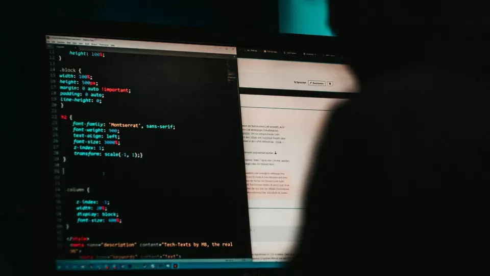 Shadowy person sitting in front of two computer screens