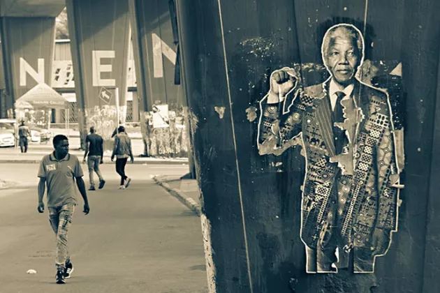 Man walking behind photo of Nelson Mandela