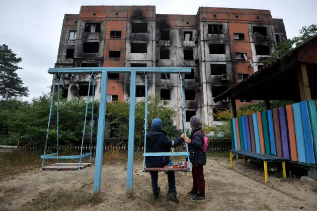 Children stand on a playground in front of a destroyed building in Kalynivka, north of Kyiv. Photo: Sergei Chuzavkov/AFP.