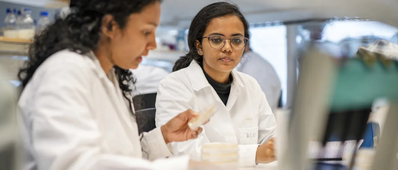 Two students in lab coats discussing.