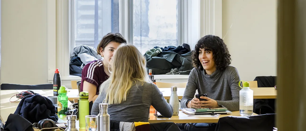 Three students sitting in a sunny classroom and talking. Photo.
