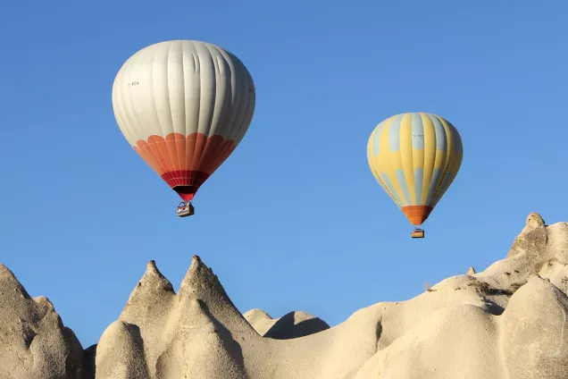 Two hot air balloons above pointy rocks and against a blue sky.