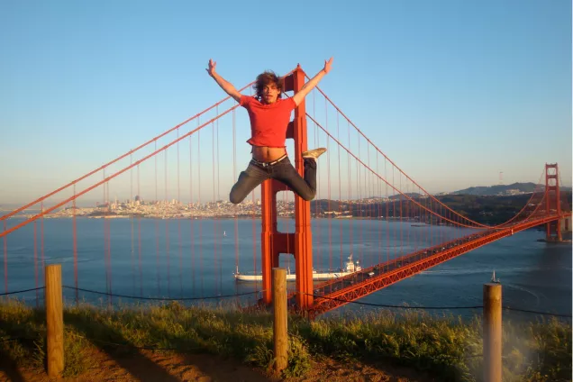 A student jumping in front of the Golden Gate Bridge. Photo.