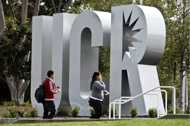 Two students passing by the giant letters UCR, 'UC Riverside'. Photo.