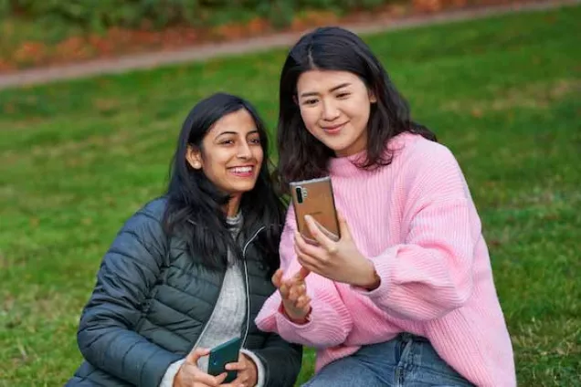 Two students looking at a phone together. Photo.