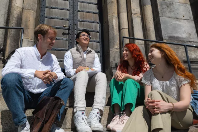 Four students talking and laughing in front of Lund Cathedral. Photo.
