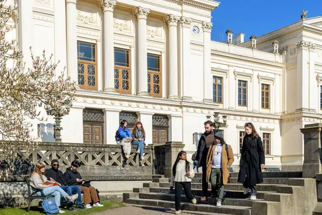 Students in front of the University's main white building on a sunny day. Photo.