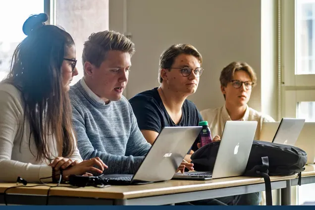 A group of students seated in a classroom, listening and taking notes during a lecture. Photo.