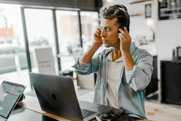 A person wearing headphones working on a laptop at a desk. Photo.