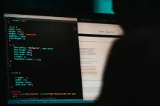 Shadowy person sitting in front of two computer screens