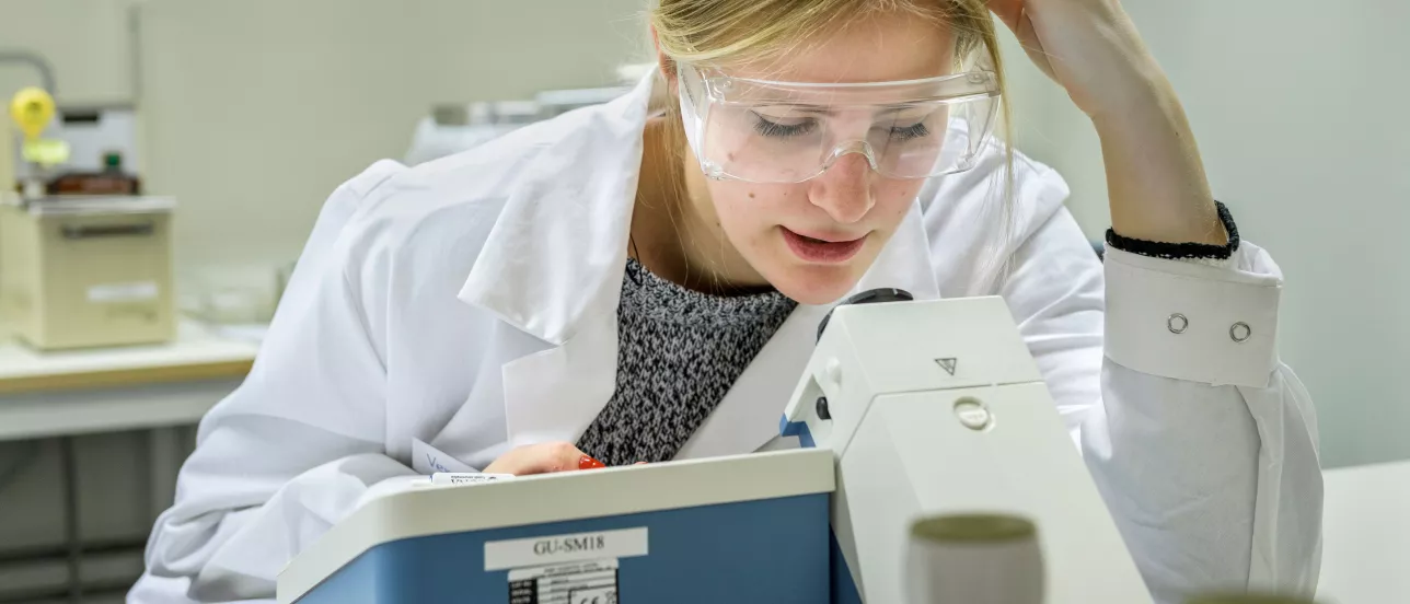 A girl looking into a microscope with safety glasses on