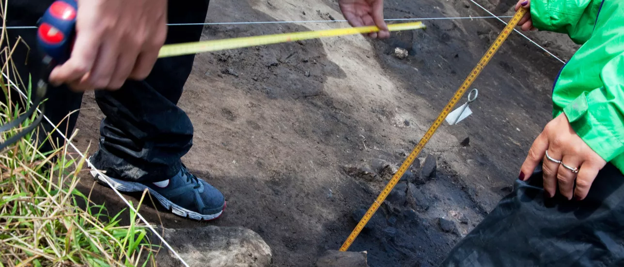 Hands measuring something at an archaeological excavation