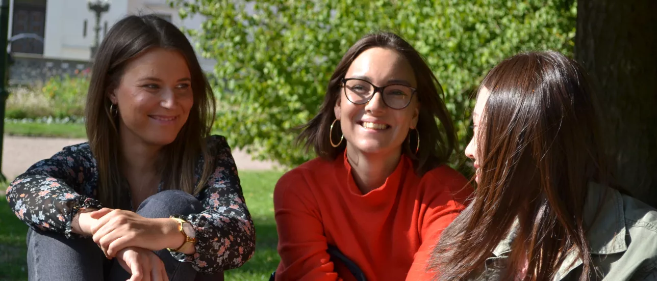 Three students laughing on the grass near the Main University Building