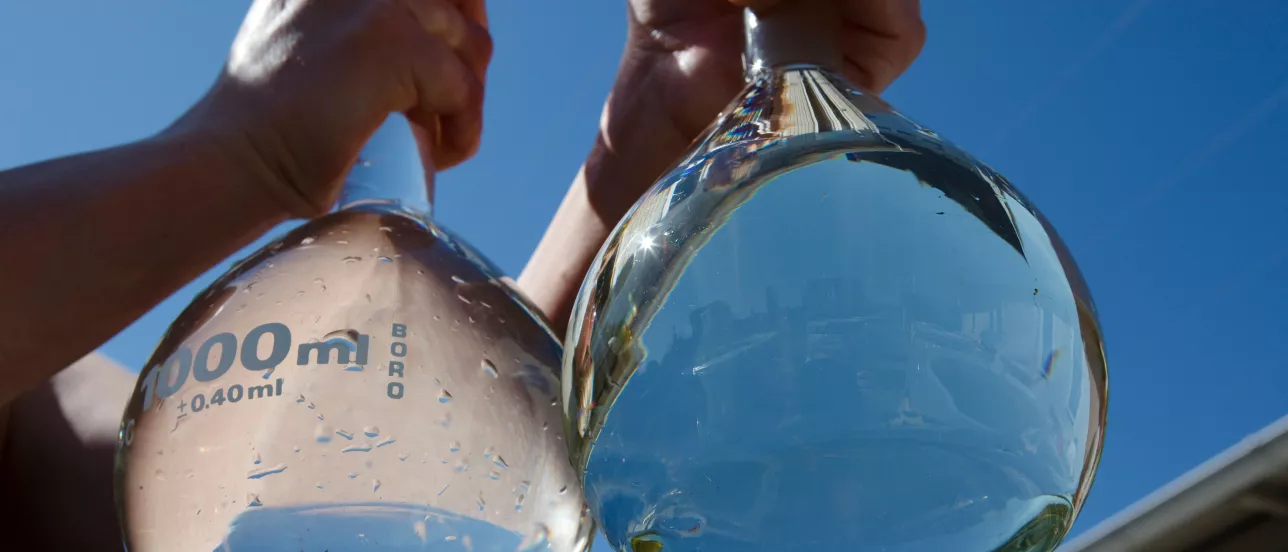 Someone holding two transparent tanks of water against a blue sky