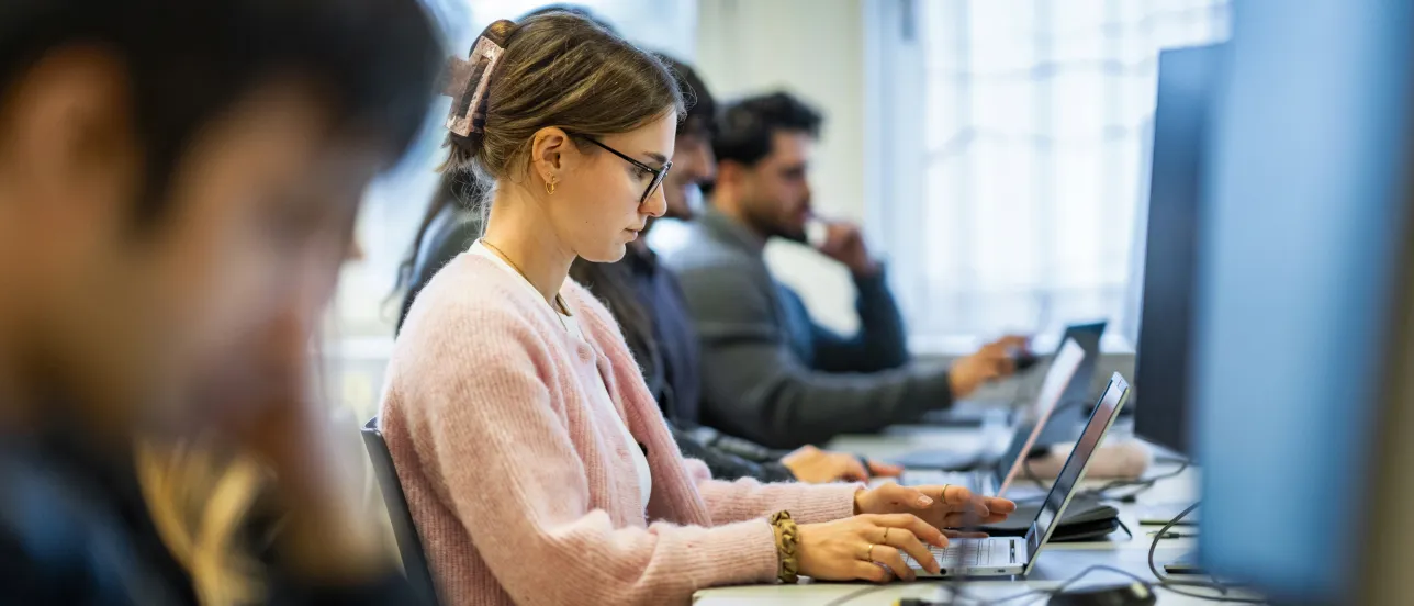 Student in computer lecture room on laptops, photo from the side with one person in focus. Photo