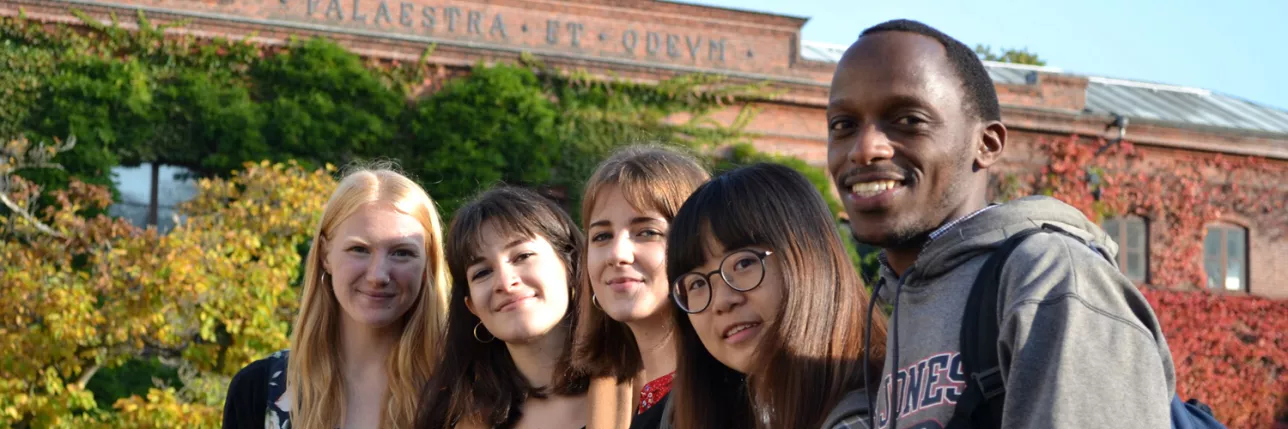 International students posing in front of the Palaestra building in autumn. Photo.