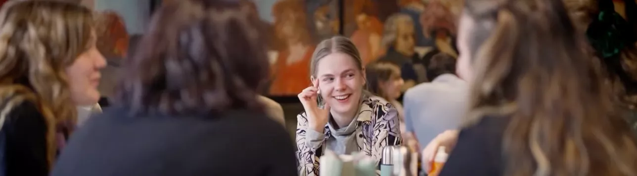 Students laughing and talking in a lunchroom with wall decorations at the Faculty of Fine and Performing arts. Photo.