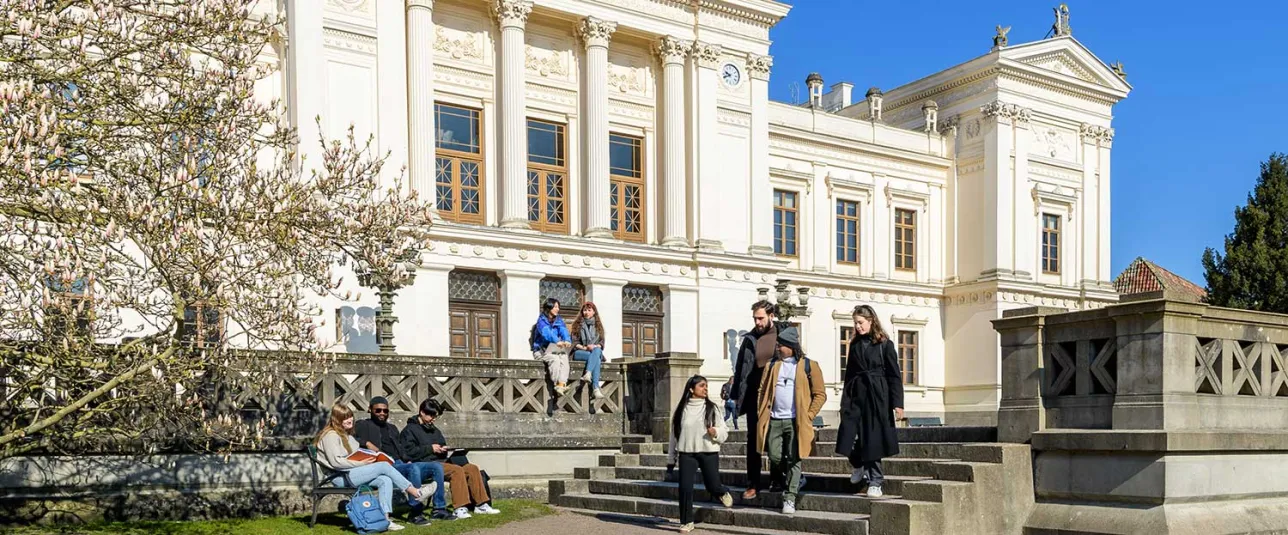 Students in front of the University's main white building on a sunny day. Photo.