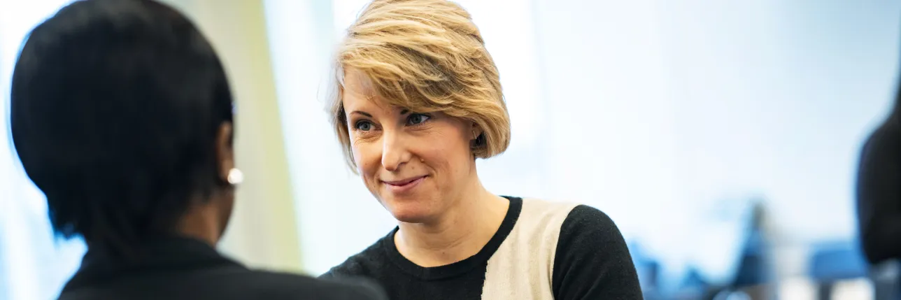 Two people having a conversation in an office-like meeting room. Photo.