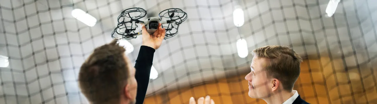 Two people interacting with a drone inside a netted indoor area. Photo.