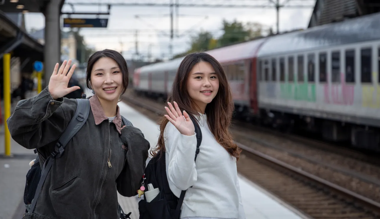Two students waving at a trainstation. Photo.