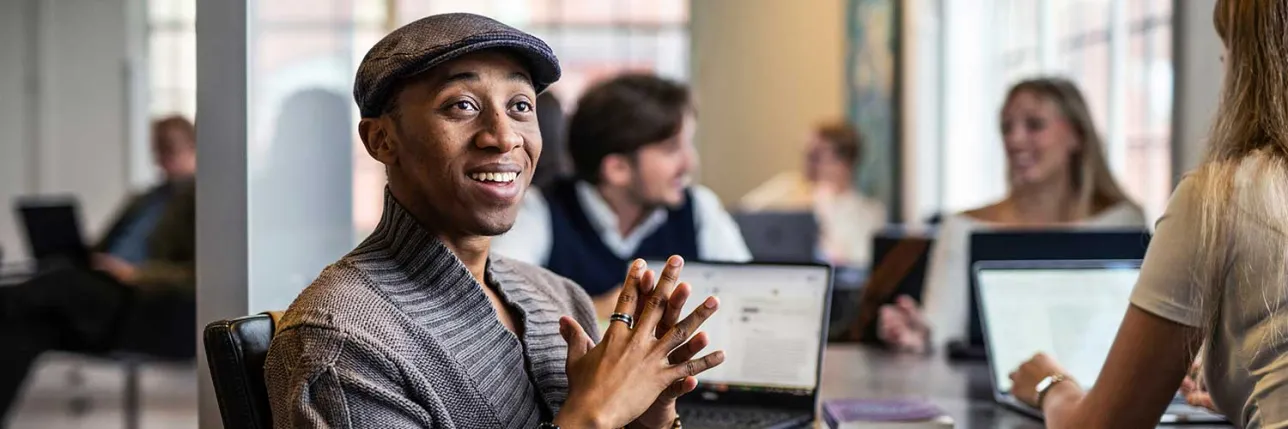 A student talking with other students in the background. Photo.