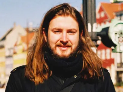 Portrait photo of a man standing in front of a blurry city background.
