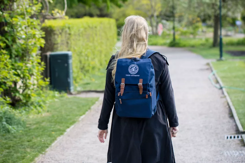 A student walking in the Botanical Garden wearing an LU bag