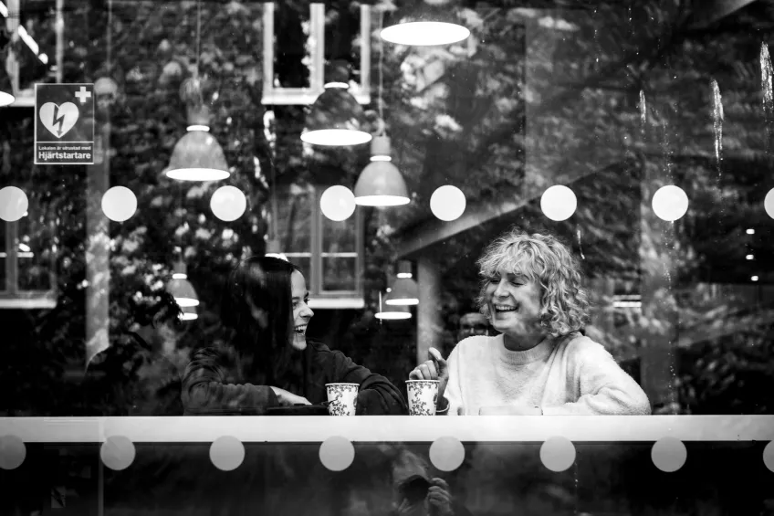 Students laughing and drinking coffee at a cafe, seen through the window