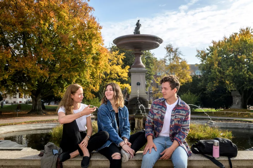 Three students talking and laughing in front of the fountain in autumn
