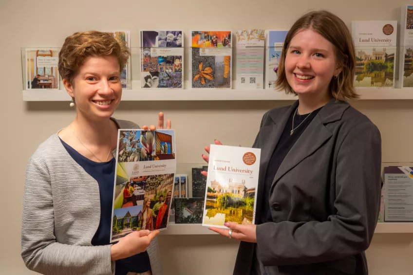 Two employees at the International Desk posing with university brochures. Photo.