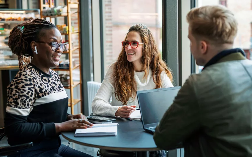 Three students studying around a table. Photo.